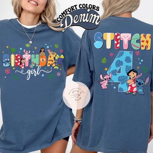 May include: Denim blue t-shirt with a colorful graphic featuring characters and text. The front of the shirt says "Birthday girl" with character illustrations. The back says "Stitch 4" with character illustrations. The shirt has short sleeves and a crew neck.