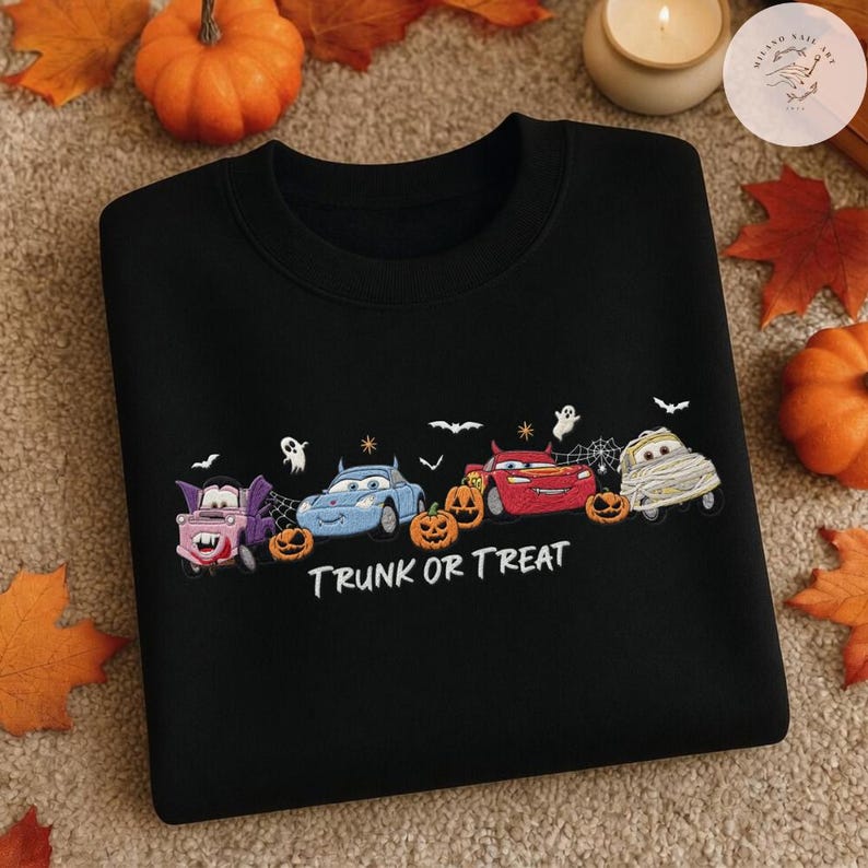 May include: A black crewneck sweatshirt featuring an embroidered graphic of four cartoon cars dressed in Halloween costumes, including a vampire, a devil, and a mummy, alongside pumpkins, ghosts, and bats, with the white text TRUNK OR TREAT.