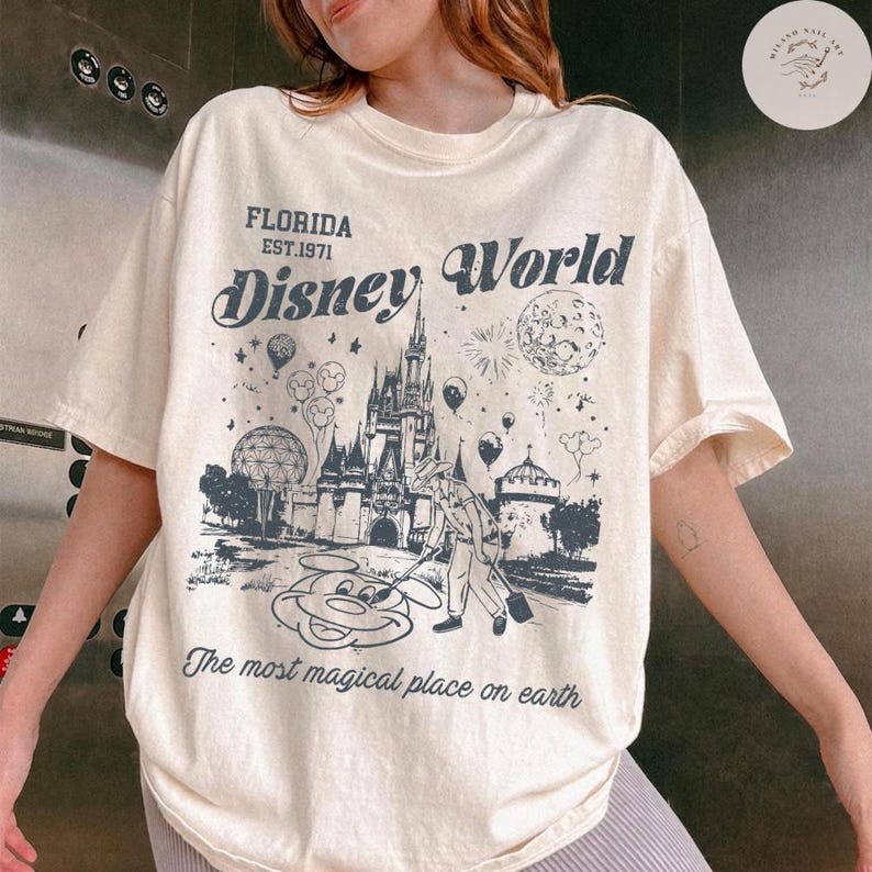 Może przedstawiać: Kremowa koszulka z grafiką Disney World, w tym zamkiem, Myszka Miki i napisem "Florida Disney World". Koszulka zawiera r&oacute;wnież frazę "The most magical place on earth."