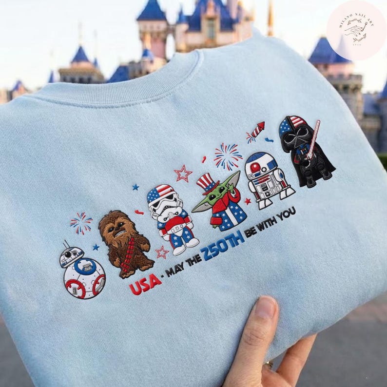 Op de afbeelding: Lichtblauw sweatshirt met geborduurde Star Wars-personages in patriottische kleding. Het ontwerp bevat Darth Vader en R2-D2, met de tekst "USA - MAY THE 250TH BE WITH YOU".