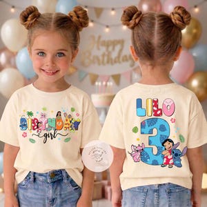 May include: A cream-colored t-shirt with a colorful "Birthday girl" design on the front and "Lilo 3" on the back. The front design includes cartoon characters and the text "Birthday girl". The back features the name "Lilo" and the number "3".
