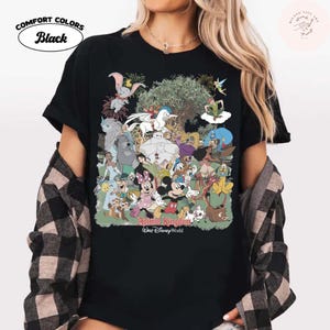 Puede incluir: Camiseta negra Comfort Colors con un gr&aacute;fico colorido de varios personajes de Disney, incluyendo Mickey y Minnie Mouse, Dumbo, y otros. Las palabras "Animal Kingdom" y "Walt Disney World" est&aacute;n impresas debajo.