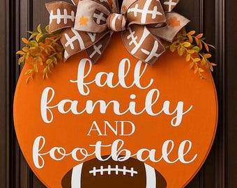 May include: A round orange wooden door sign featuring the white text fall family AND football and a brown football graphic at the bottom. The sign is topped with a large decorative bow patterned with footballs and autumn leaves, plus green foliage.