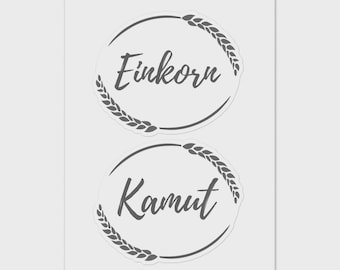 May include: Two circular stickers with the words "Einkorn" and "Kamut" in a handwritten font. Each sticker has a wheat stalk design around the edge, and the background is a light gray.