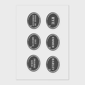 May include: A sheet of six oval stickers with dark grey backgrounds and white text. The stickers are labelled with various grains: Rye, Emmer, Barley, Oat Groats, Prairie Gold, and Rouge de Bordeaux. Each sticker has a decorative leaf design.
