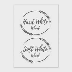 Peut inclure: Deux autocollants circulaires avec des bordures d'épis de blé. L'autocollant supérieur indique "Hard White Wheat" dans une police cursive. L'autocollant inférieur indique "Soft White Wheat". Les deux autocollants sont sur fond blanc.