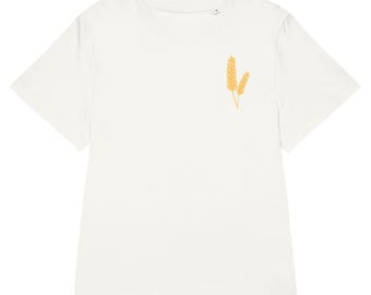 May include: A white t-shirt with a crew neck and short sleeves. The shirt features a small, embroidered design of two wheat stalks in a golden yellow color on the left chest. The shirt is made of a soft, likely organic material.