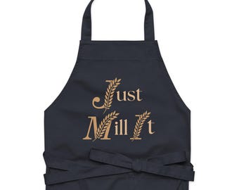 May include: A navy blue apron with the text "Just Mill It" in a gold color, with wheat stalk illustrations. The apron has a neck loop and waist ties.