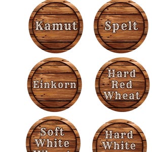 May include: Six circular wooden labels displaying different wheat varieties. The labels are brown with a wood grain effect and feature text in a serif font. The labels read: Kamut, Spelt, Einkorn, Hard Red Wheat, Soft White Wheat, and Hard White Wheat.