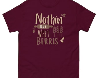 May include: A maroon short-sleeve t-shirt featuring the text Nothin BUT WEET BERRIS in light tan and brown lettering. The design includes a brown rolling pin graphic, three wheat stalks, and small decorative brown splashes.