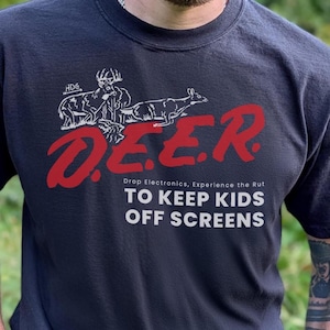 Peut inclure: Un t-shirt bleu marine foncé avec un graphisme en lignes blanches représentant deux cerfs, le texte rouge D.E.E.R. et le texte blanc Drop Electronics, Experience the Rut TO KEEP KIDS OFF SCREENS imprimé sur le devant du vêtement.