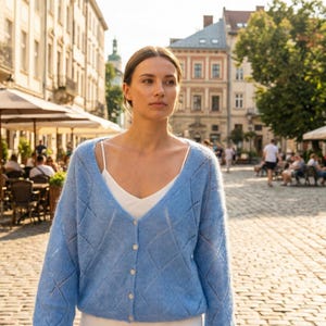 May include: A light blue cardigan with a diamond pattern and button closure. The cardigan is worn over a white camisole. The image is taken outdoors with a blurred background of a city street.