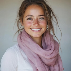 Może przedstawiać: Kobieta z jasnobrązowymi włosami i piegami uśmiecha się, ubrana w białą koszulę i jasno fioletowy szal. Szal jest udrapowany wokół szyi i ramion.