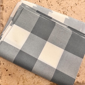 Puede incluir: Un trozo de tela doblado con un patrón de cuadros grises y blancos. La tela está doblada en tres partes y los bordes son visibles.