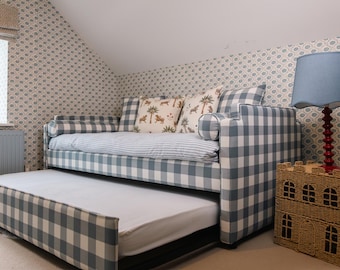 Cama individual tapizada en tela de cuadros azules con cama nido extraíble.