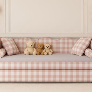 May include: A daybed with a pink and white gingham pattern, featuring three teddy bears and two matching pillows. The bed has a scalloped back and is set against a neutral wall with sconces.