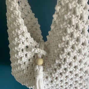 May include: White macrame hanging planter with a wooden bead and a tassel. The planter is made of cotton rope and has a diamond pattern.