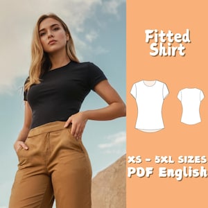 Op de afbeelding: Een vrouw draagt een zwart getailleerd T-shirt en een bruine broek. De afbeelding bevat een diagram van een getailleerd shirt en de tekst "Fitted Shirt" en "XS - 5XL SIZES PDF English". De achtergrond toont een lucht en een berg.