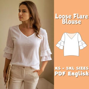Op de afbeelding: Witte losse flare blouse met een V-hals en driekwart mouwen met ruches manchetten. De afbeelding bevat een diagram van de blouse en de tekst "Loose Flare Blouse" en "XS - 5XL SIZES PDF English".