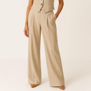 May include: Tan-colored wide-leg trousers with a matching vest. The trousers have a high waist and pleats in the front. The vest has a button closure. The outfit is made of a light-colored fabric.