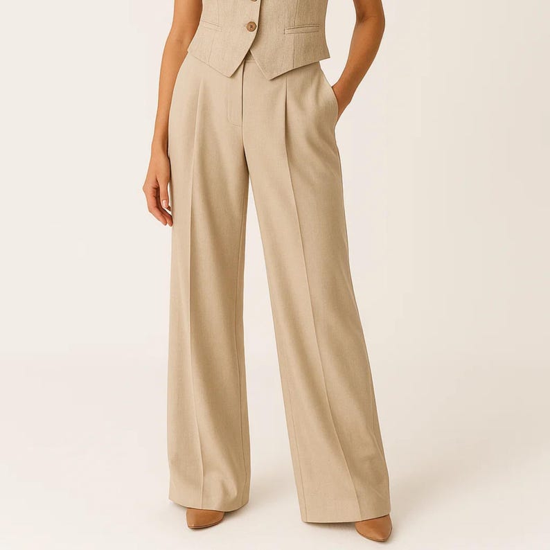 May include: Tan-colored wide-leg trousers with a matching vest. The trousers have a high waist and pleats in the front. The vest has a button closure. The outfit is made of a light-colored fabric.
