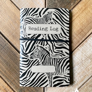 May include: A black and white zebra print notebook with the text "Reading Log" on the front cover. The notebook has a black elastic band around it.