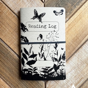 May include: A brown notebook with a black and white design featuring butterflies and foliage. The cover reads "Reading Log".