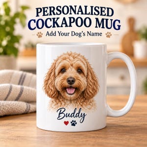 Op de afbeelding: Een witte keramische mok met een gedetailleerde illustratie van een goudbruine Cockapoo-hond. Onder de hond staat de naam Buddy in donkerblauw cursief schrift, gevolgd door een klein rood hartje en een donkerblauw pootafdrukje.