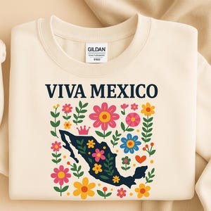 May include: Cream-colored sweatshirt with the text "VIVA MEXICO" in navy blue. The design features a navy blue outline of Mexico filled with colorful flowers and a crown, surrounded by more flowers and leaves.