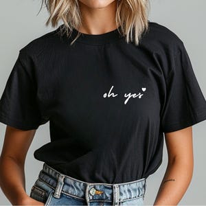 Puede incluir: Camiseta negra con texto blanco que dice "oh yes" con un peque&ntilde;o s&iacute;mbolo de coraz&oacute;n.