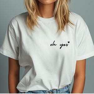 Puede incluir: Camiseta blanca con el texto "oh yes" y un peque&ntilde;o coraz&oacute;n.