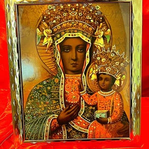 Könnte beinhalten: Eine gerahmte religiöse Ikone, die die Jungfrau Maria und das Jesuskind darstellt. Die Jungfrau Maria trägt ein dunkelblaues Gewand mit goldenen Verzierungen und eine Krone aus Gold und Juwelen. Das Jesuskind trägt ein rot-goldenes Gewand und eine Krone aus Gold und Juwelen. Der Hintergrund ist gold- und braunfarben.