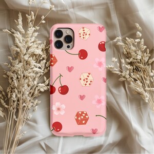 May include: A pink phone case with a pattern of dice, cherries, and hearts. The dice have red dots and the cherries are red with green stems.