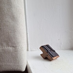 May include: A wooden printing block with a black rubber surface. The block is shaped like a letter H and has a raised design on the rubber surface.