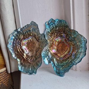 May include: Two iridescent glass plates with an organic shape. The plates have a blend of blue, gold, and brown hues, with a textured, layered appearance. The centre of each plate has a darker, more concentrated colour.