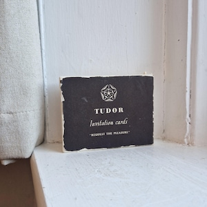 May include: A stack of Tudor invitation cards with a black background and white text. The cards feature a Tudor rose emblem and the words "TUDOR Invitation cards" and "REQUEST THE PLEASURE". The cards are on a white surface.