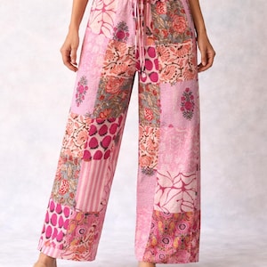 May include: Pink patchwork palazzo trousers with a drawstring waist. The trousers feature a variety of floral and geometric patterns in shades of pink, peach, and grey. The wide-leg design is visible, and the trousers are worn with sandals.