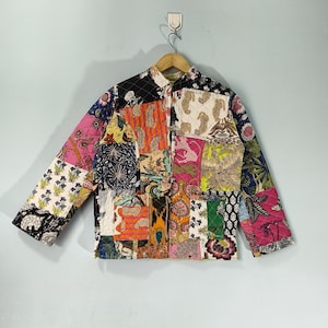 May include: A patchwork jacket with a variety of floral and animal print patterns in pink, orange, green, and blue. The jacket is quilted and has a mandarin collar and long sleeves. It is hanging on a wooden hanger.