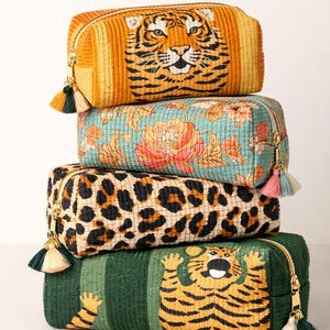 May include: Four rectangular cosmetic bags stacked on top of each other. The top bag is orange with a tiger face. The second bag is teal with a floral pattern. The third bag is leopard print. The bottom bag is green with a tiger graphic.