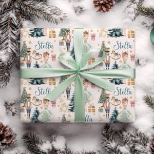 以下が含まれることがあります： 明るい緑色のリボンで結ばれたギフト。包装紙には、クリスマスツリー、くるみ割り人形、バレリーナ、そして「Stella」という名前が繰り返されるパターンで描かれています。背景は雪の効果がある白です。