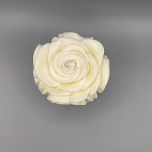 Pu&ograve; includere: Una candela bianca a forma di rosa con un design dettagliato e stratificato.