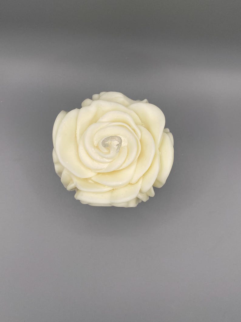 Pu&ograve; includere: Una candela bianca a forma di rosa con un design dettagliato e stratificato.