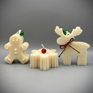 Può includere: Tre candele natalizie color avorio: un omino di pan di zenzero, un fiocco di neve e una renna. Ogni candela ha uno stoppino ed è adornata con piccole campane e nastri festivi. La renna ha un nastro rosso e verde legato alle corna.