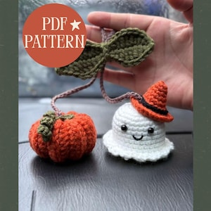 Pode incluir: Decorações de Halloween de crochê, incluindo uma abóbora laranja e um fantasma branco usando um chapéu de bruxa. O fantasma tem um rosto sorridente. O texto "PDF PATTERN" está em um círculo no canto superior esquerdo.