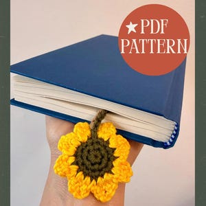 May include: A blue hardcover book with a handmade crochet sunflower bookmark. The bookmark features a yellow sunflower with a green center and a brown stem. The text "PDF PATTERN" is in a red circle.