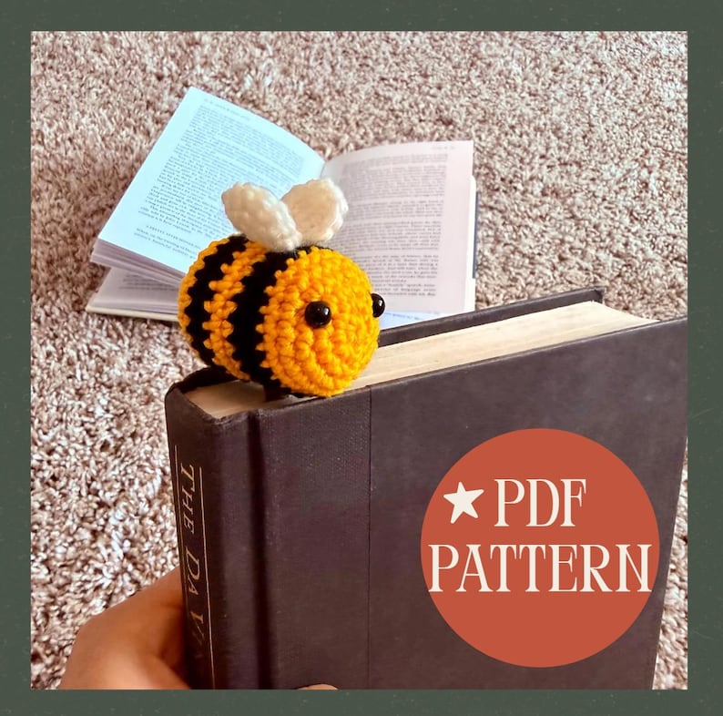 May include: A handmade crochet bee bookmark in yellow and black stripes with white wings, resting on a book. The book has the text "THE DA". A red circle with the text "PDF PATTERN" is visible.