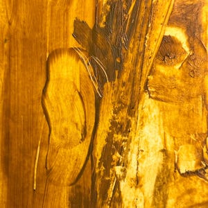 May include: Abstract artwork with a textured surface. The painting features a blend of golden yellow and brown hues, with visible brushstrokes and a layered effect. The artwork has a warm, earthy tone.