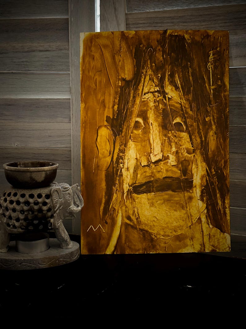 May include: Abstract oil painting on canvas, featuring a face with a neutral expression. The artwork uses shades of brown and gold, with visible brushstrokes. A small, carved elephant statue and a decorative bowl are in the foreground.