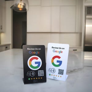 May include: Two small, rectangular signs with the text "Review Us on Google." One sign is black, the other white. Both feature the Google logo and a QR code. The black sign has a five-star rating graphic.
