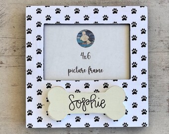 May include: A white 4x6 picture frame with a paw print pattern. The frame has a bone-shaped accent with the name "Sophie" in script. The frame is designed for pet photos.
